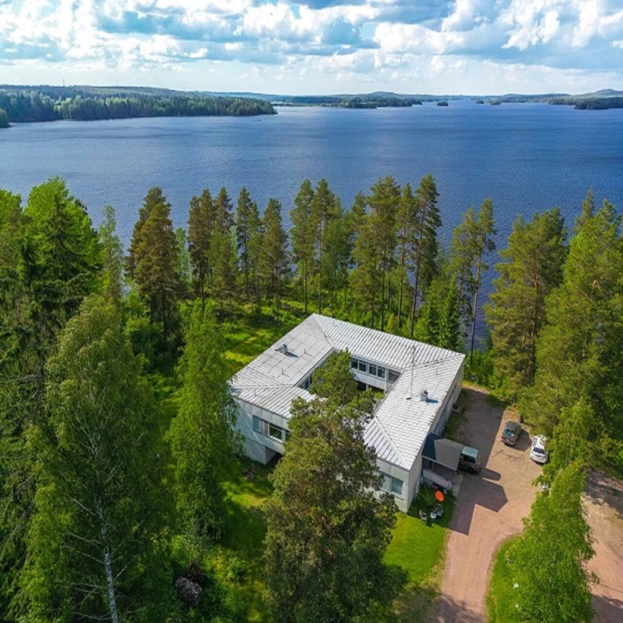 Ilmakuva Vinsanvillasta, joka sijaitsee järven rannalla ja jossa näkyvät maalaukselliset luontomaisemat sekä rakennuksen ainutlaatuinen arkkitehtuuri