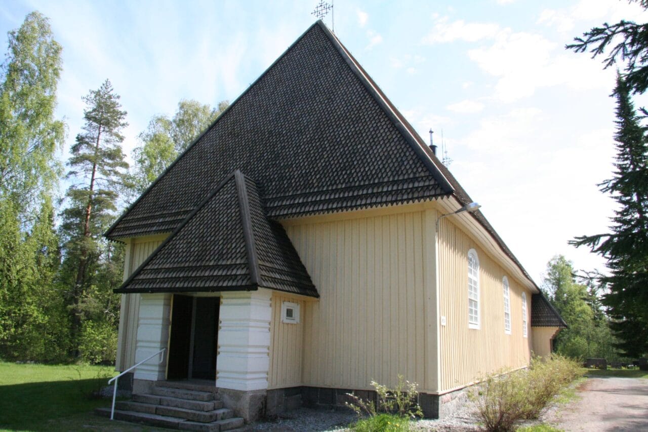 Aurejärven kirkko kuvattuna ulkoapäin. Rakennus on muodoiltaan pelkistetty, matalahko puurakennus, jossa on kermanvalkea verhoilu ja ruskeanharmaa viistokatto.