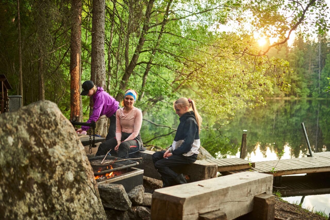 Nuotiopaikalla Ruutanajärven rannalla nainen ja kaksi lasta grillaavat.