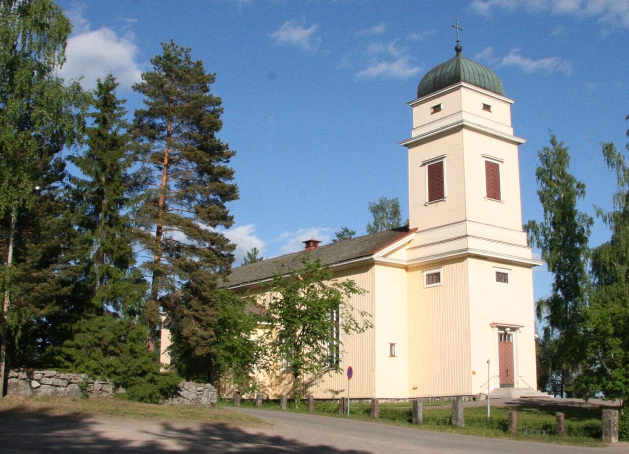 Viljakkalan kirkko kuvattuna kesällä ulkoapäin. Kirkko on kermanvaalea ja suoralinjainen rakennus, jonka kuvaa lähemmässä päädyssä kohoaa korkea torni.
