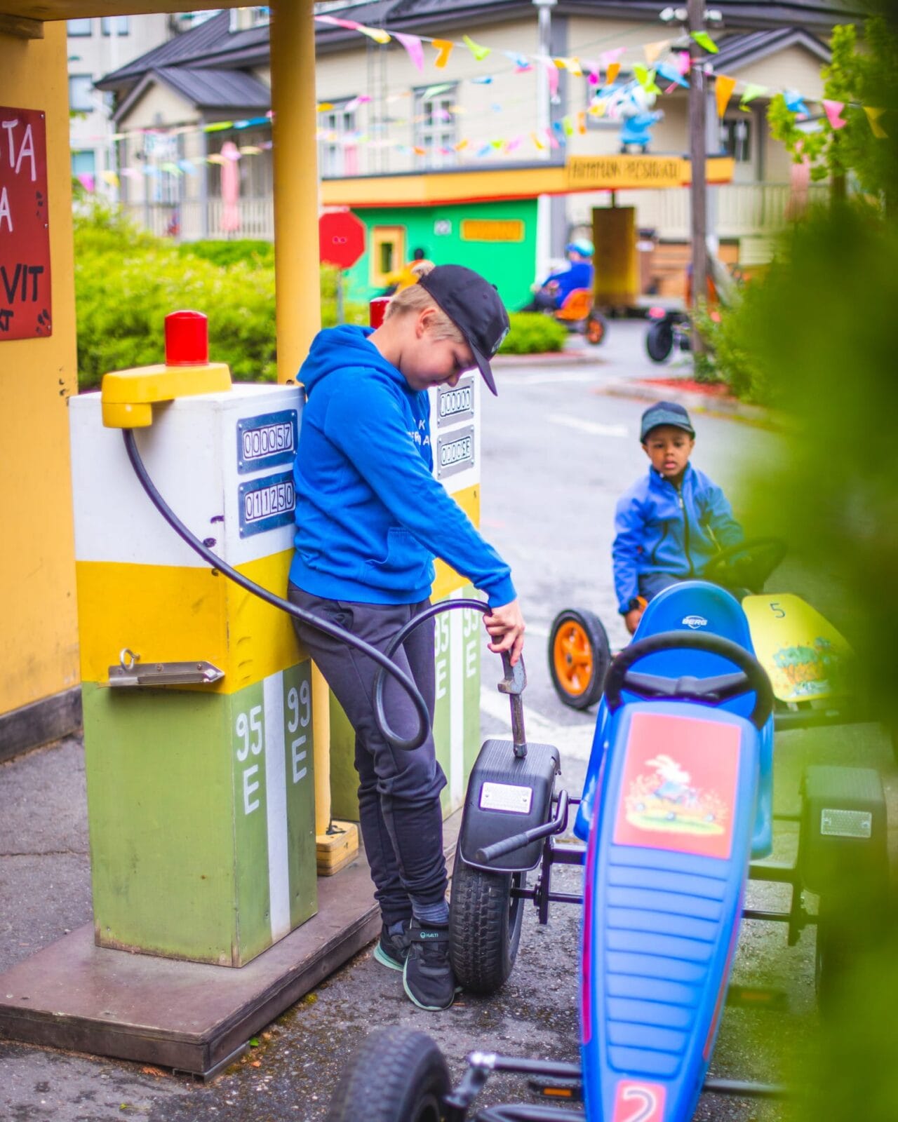 A child has driven his pedal car to the fuel station and is pretending to fill up the tank.