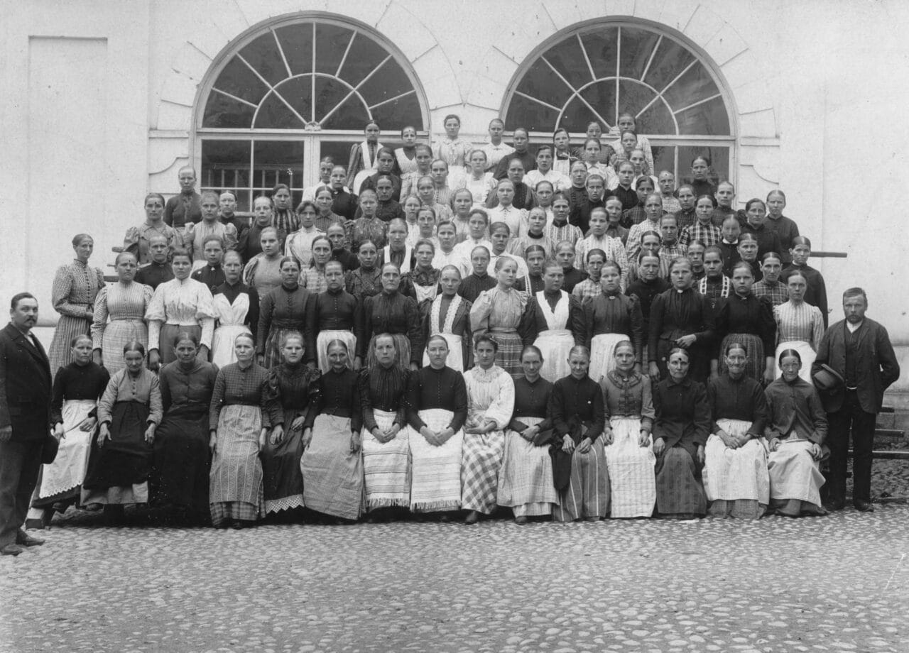 A black-and-white piciture of female factory workers in long aprons.
