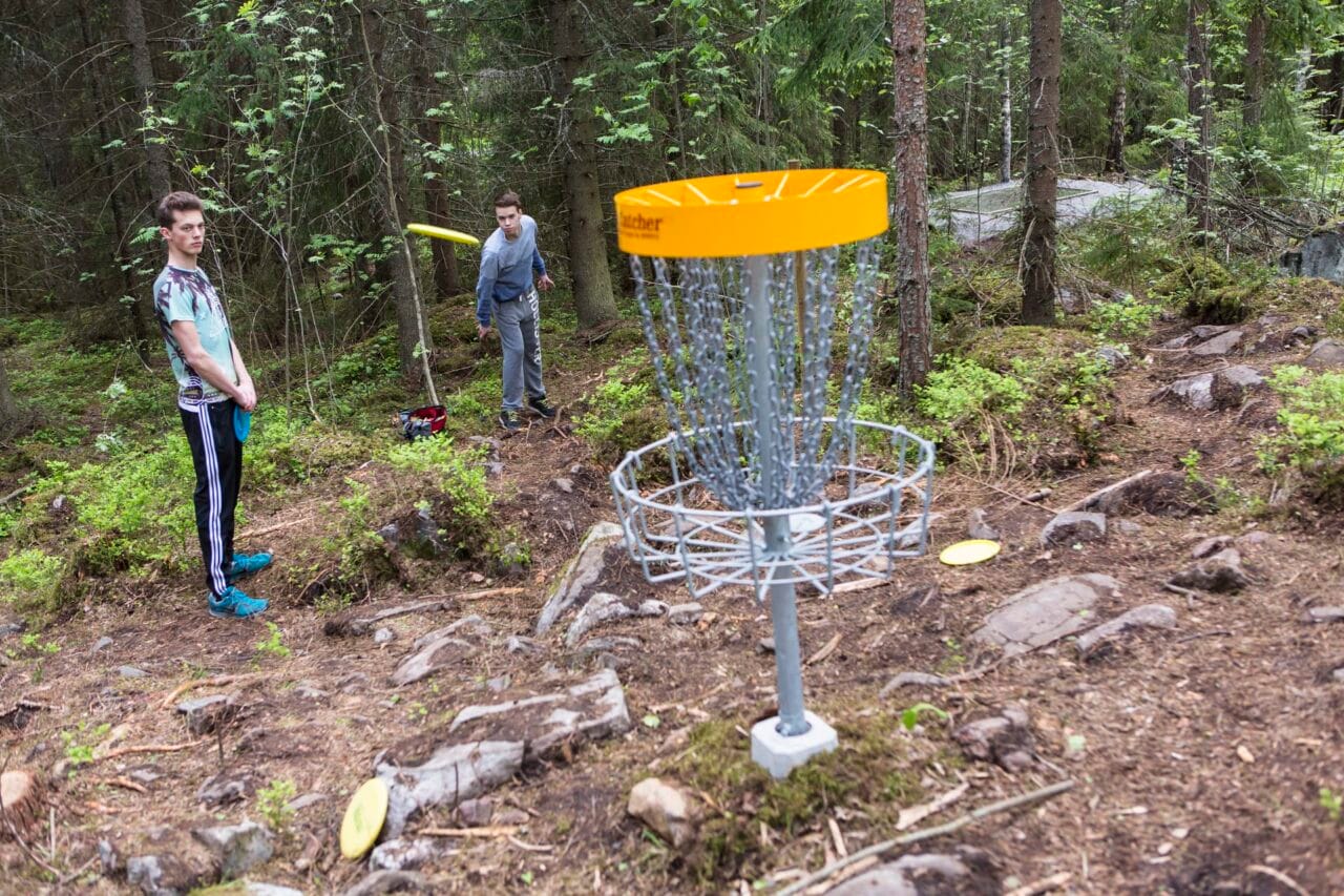 Henkilöt heittävät frisbeegolfia maaliin.