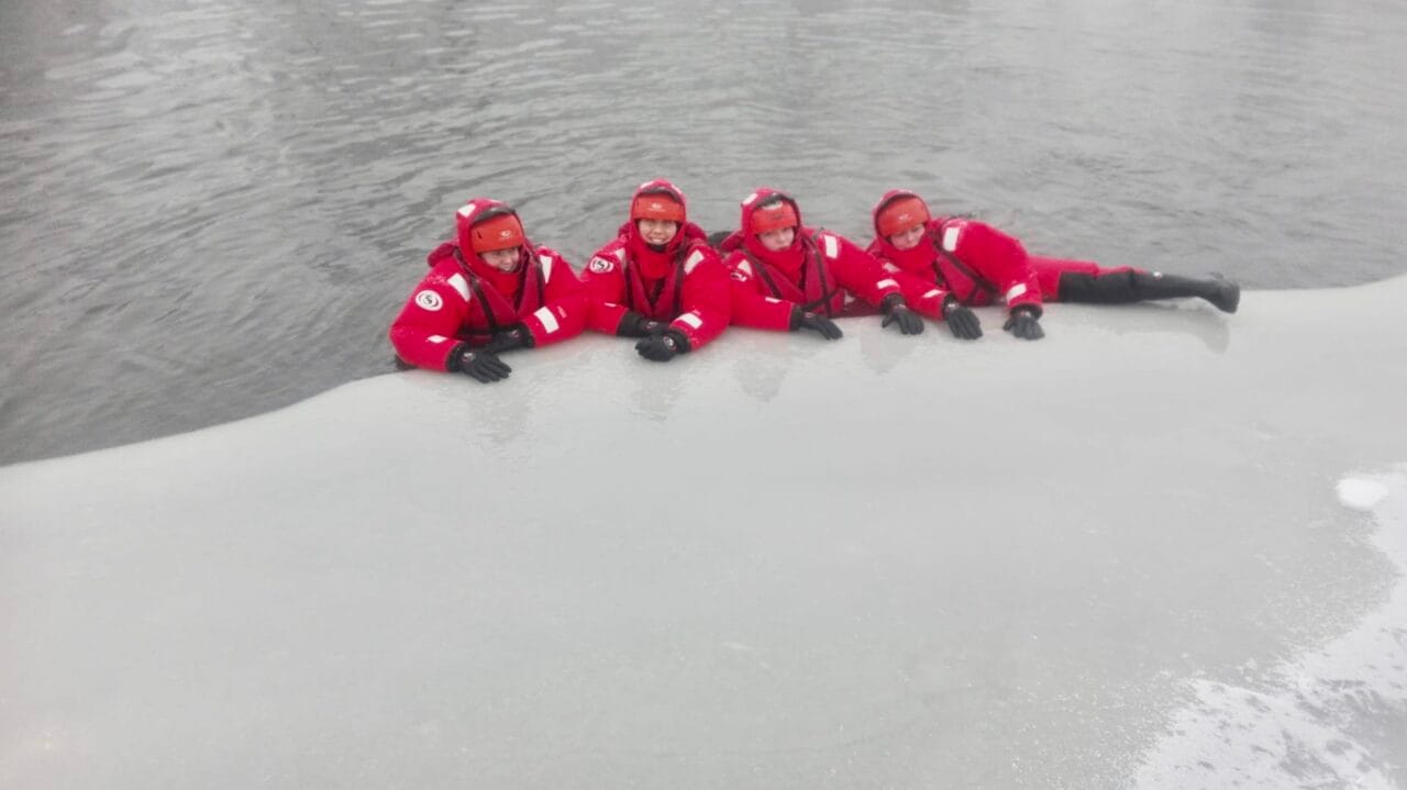People in survival suits at the edge of the ice.
