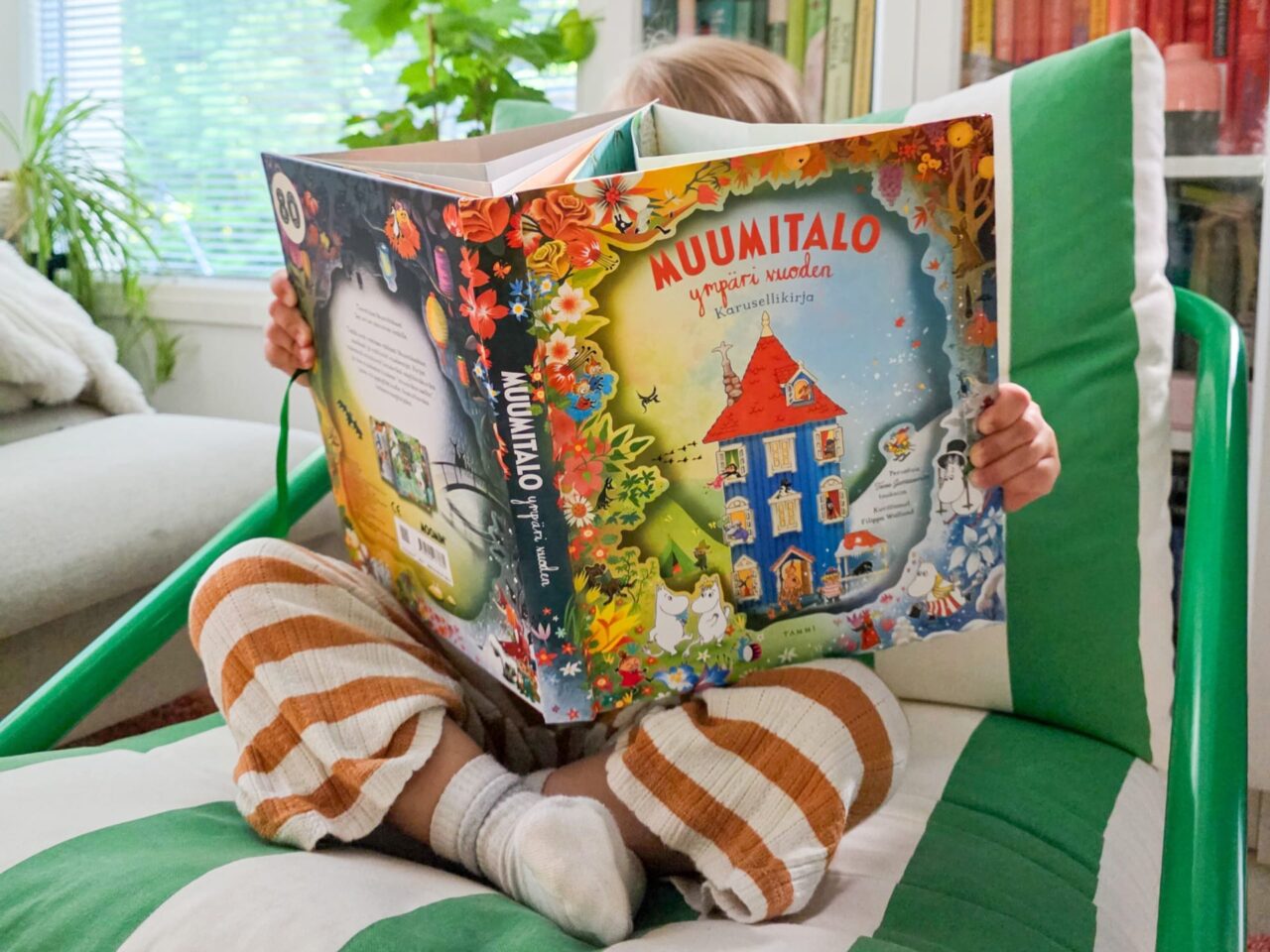 Lapsi lukemassa muumikirjaa sohvalla
